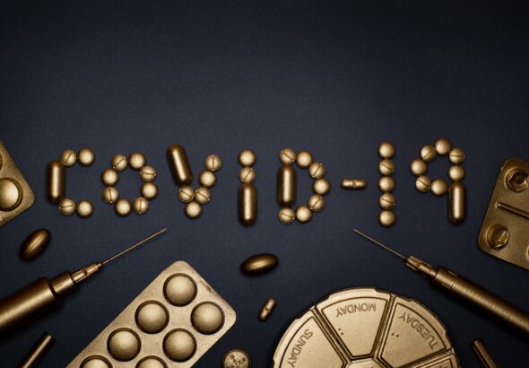 Creative COVID-19 concept with gold pills and syringes arranged on a dark background.