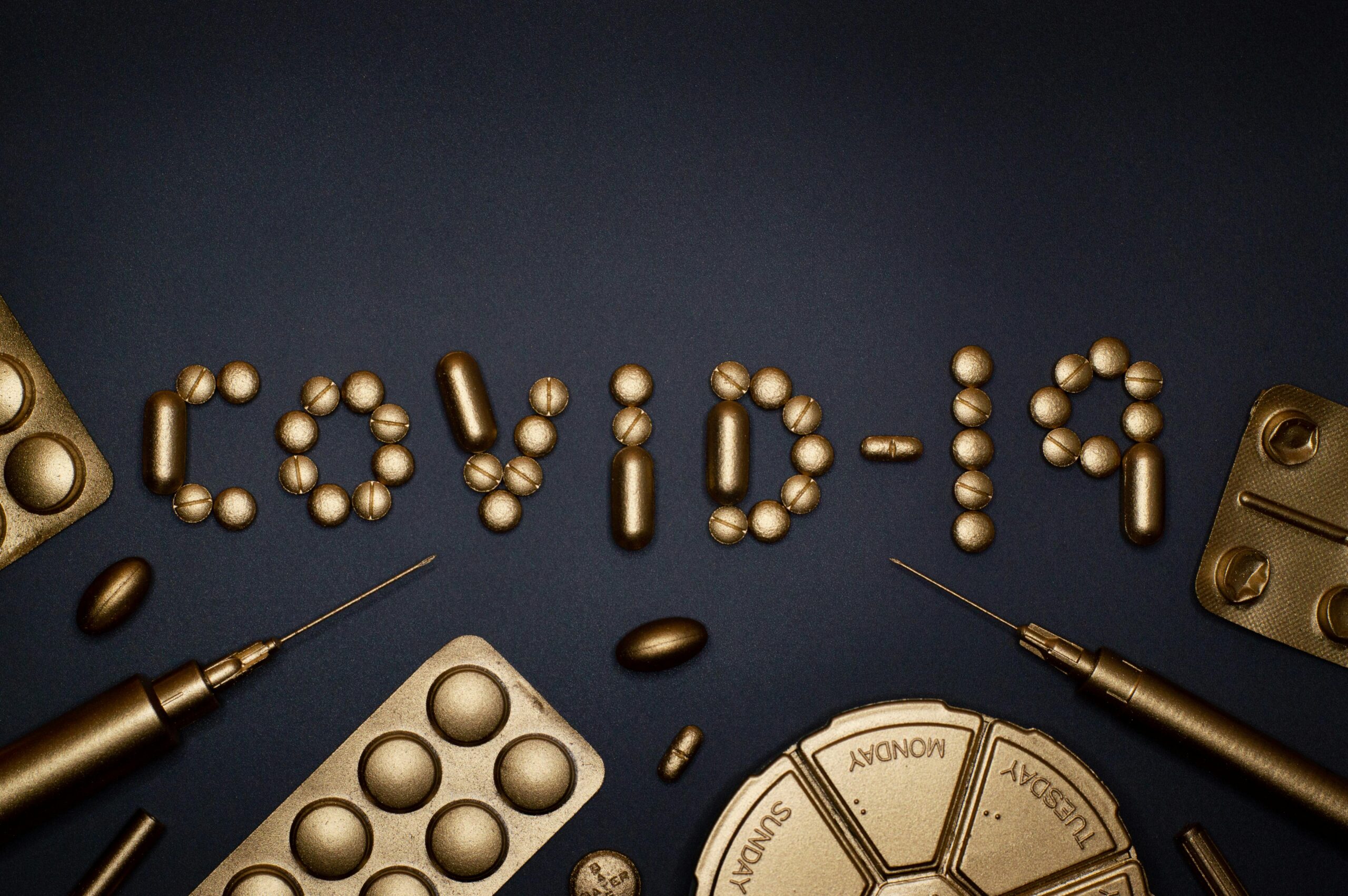 Creative COVID-19 concept with gold pills and syringes arranged on a dark background.