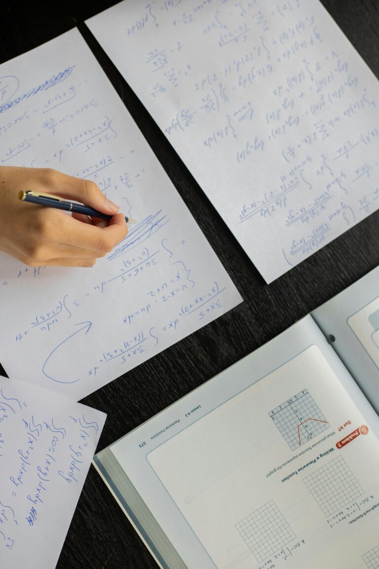 Close-up of a student solving mathematical equations with papers and textbook on a table.cetonline.karnataka.gov.in 2025