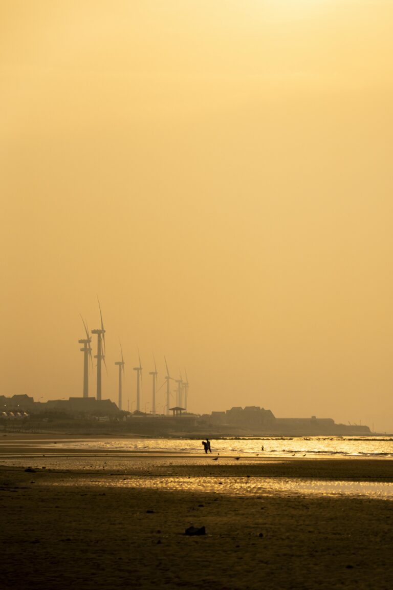 Silhouetted wind turbines along a golden seaside during sunset, evoking tranquility and renewable energy. बारिश मौसम विभाग