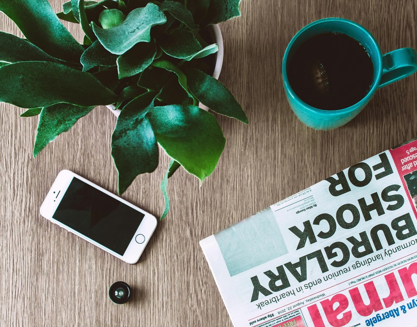 Flat lay arrangement of a coffee mug, newspaper, smartphone, and plant on a wooden table. BREAKING NEWS aaj ki taaja khabar