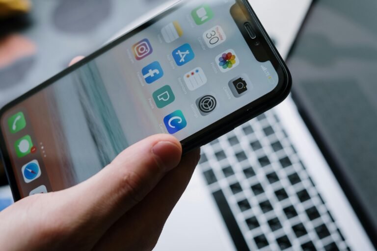 Person holding a smartphone in front of a laptop showcasing various app icons, highlighting digital connectivity. instagram reposting reels